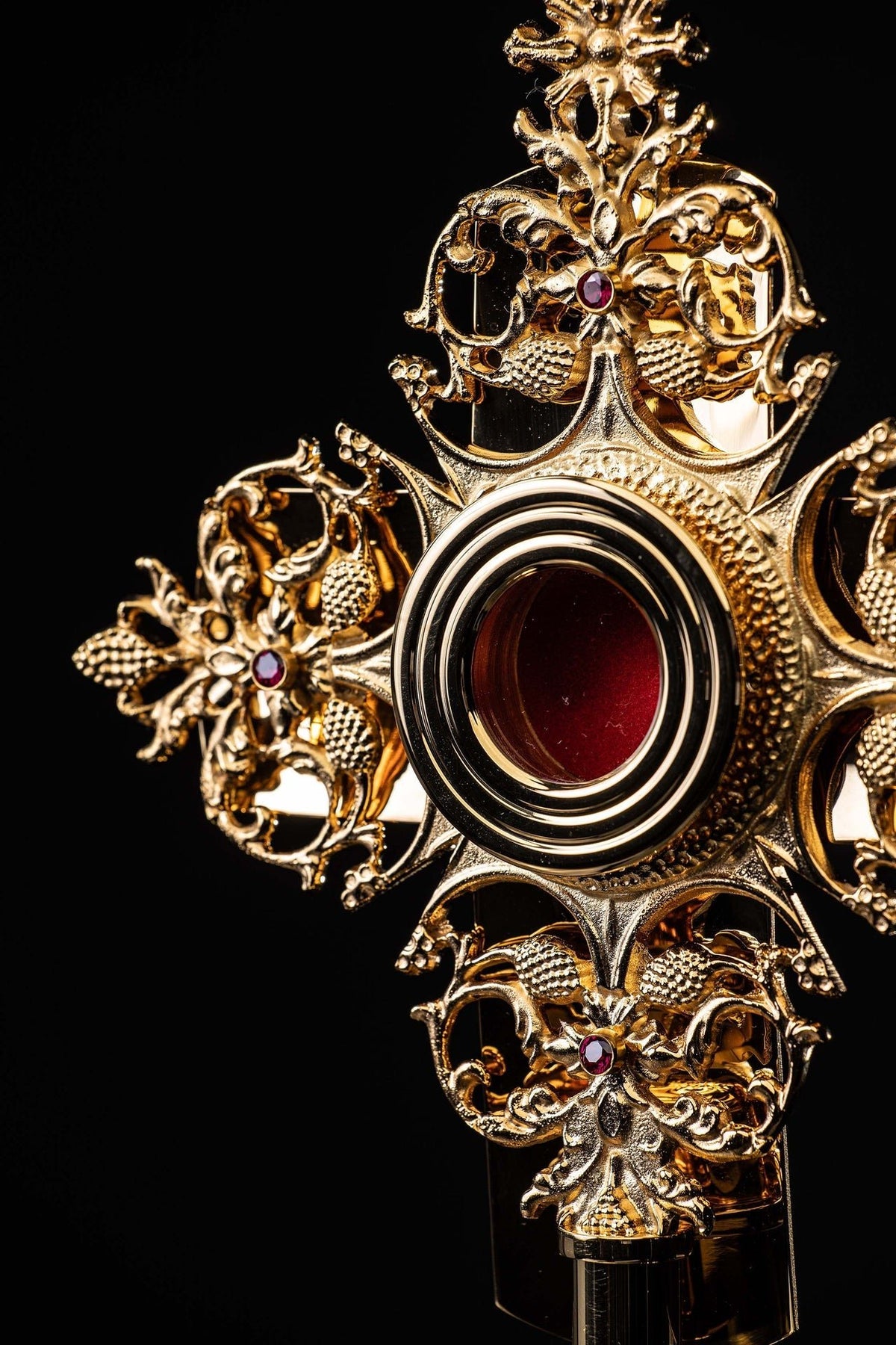 Detailed view of gilded brass reliquary with red jeweled accents and grape motifs