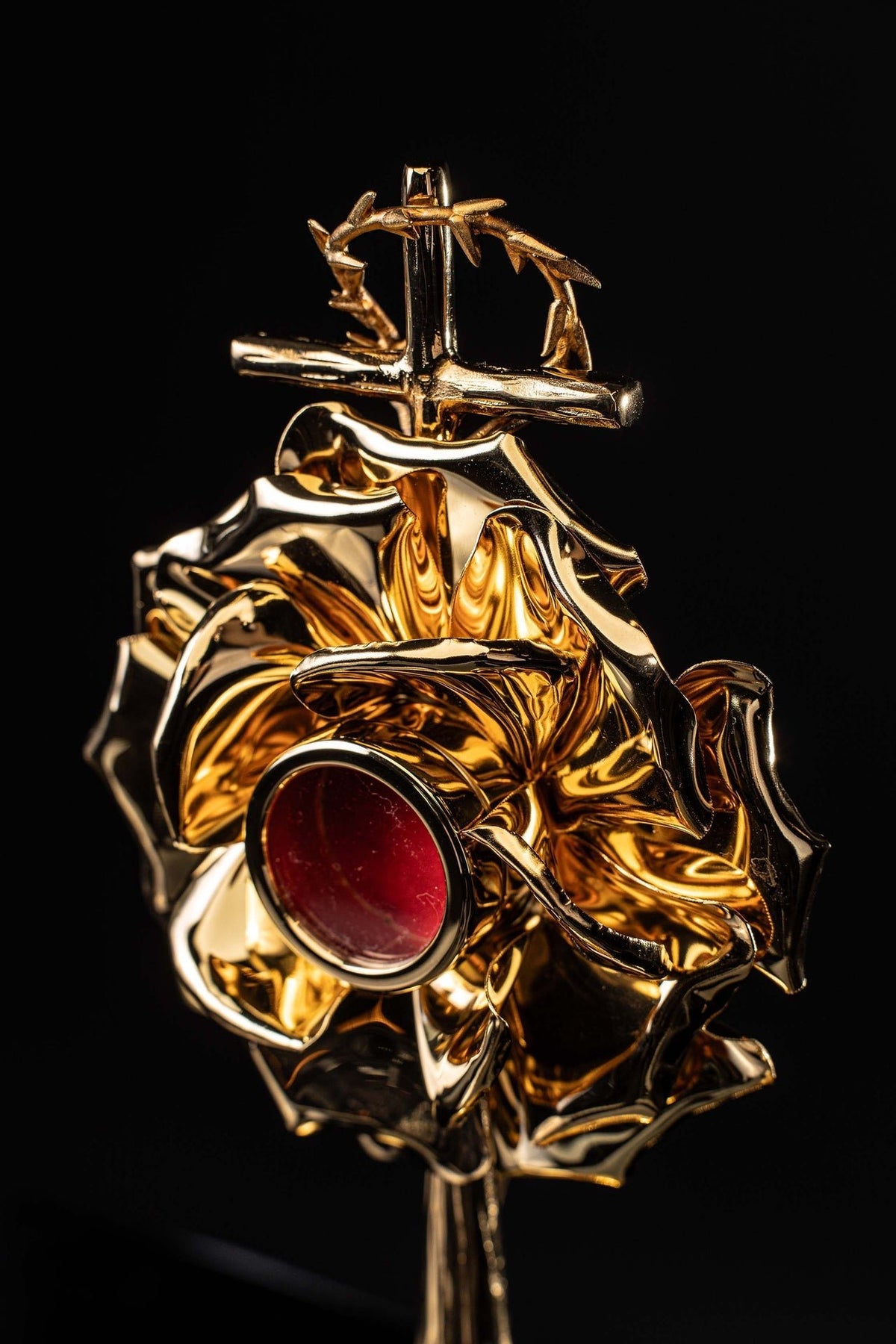 Angled view of the reliquary showing the cross finial, red medallion and gold floral relief