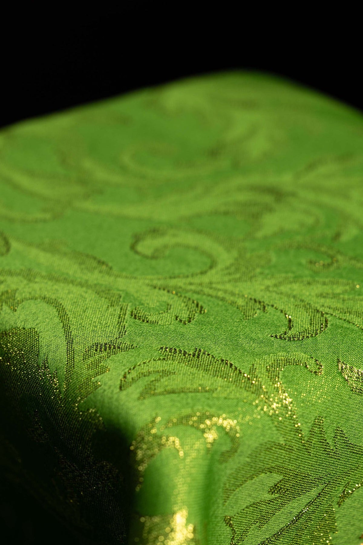 Fabric close-up of the green chalice veil with gold decorative pattern