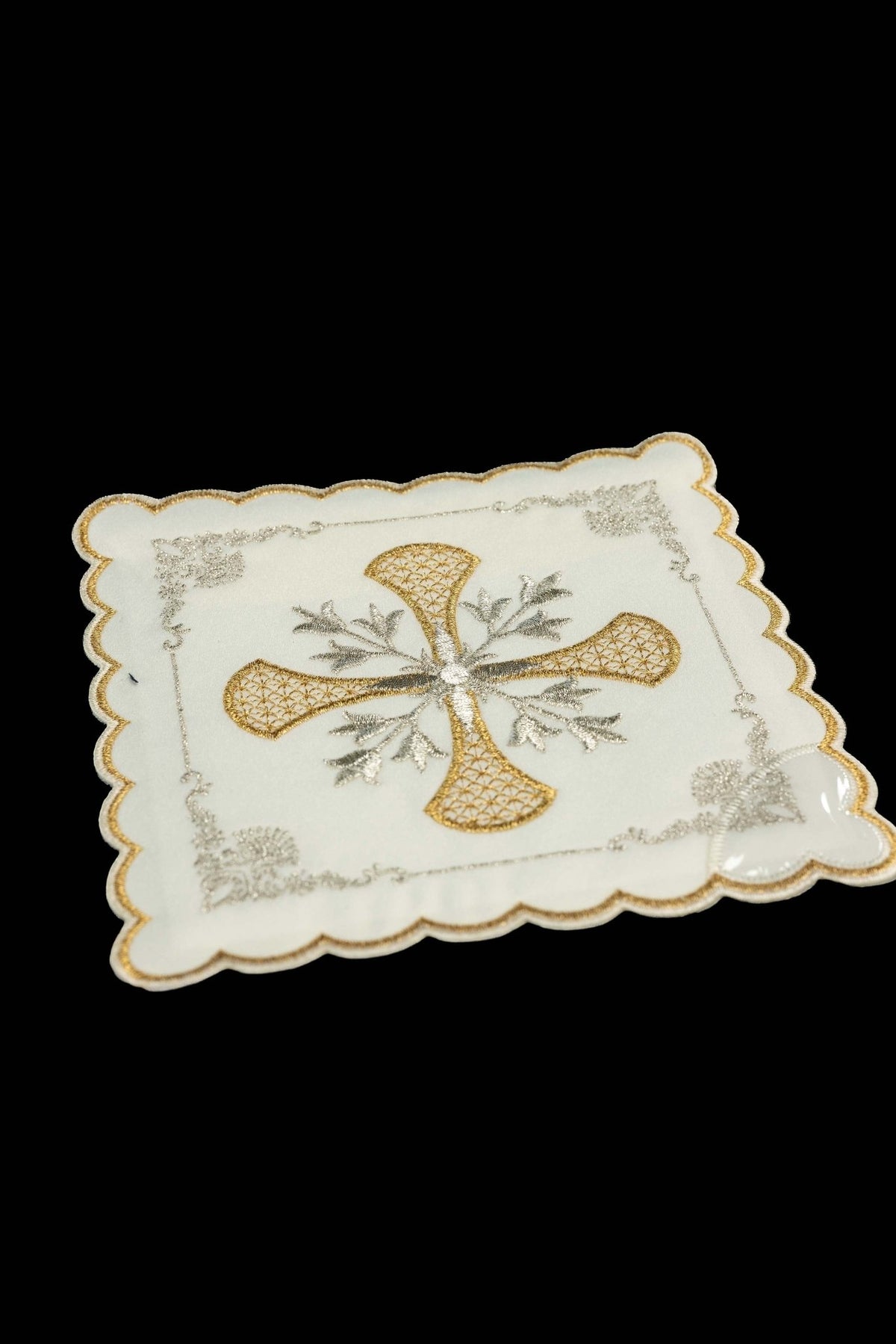 Angled view of white chalice pall with gold and silver embroidered cross