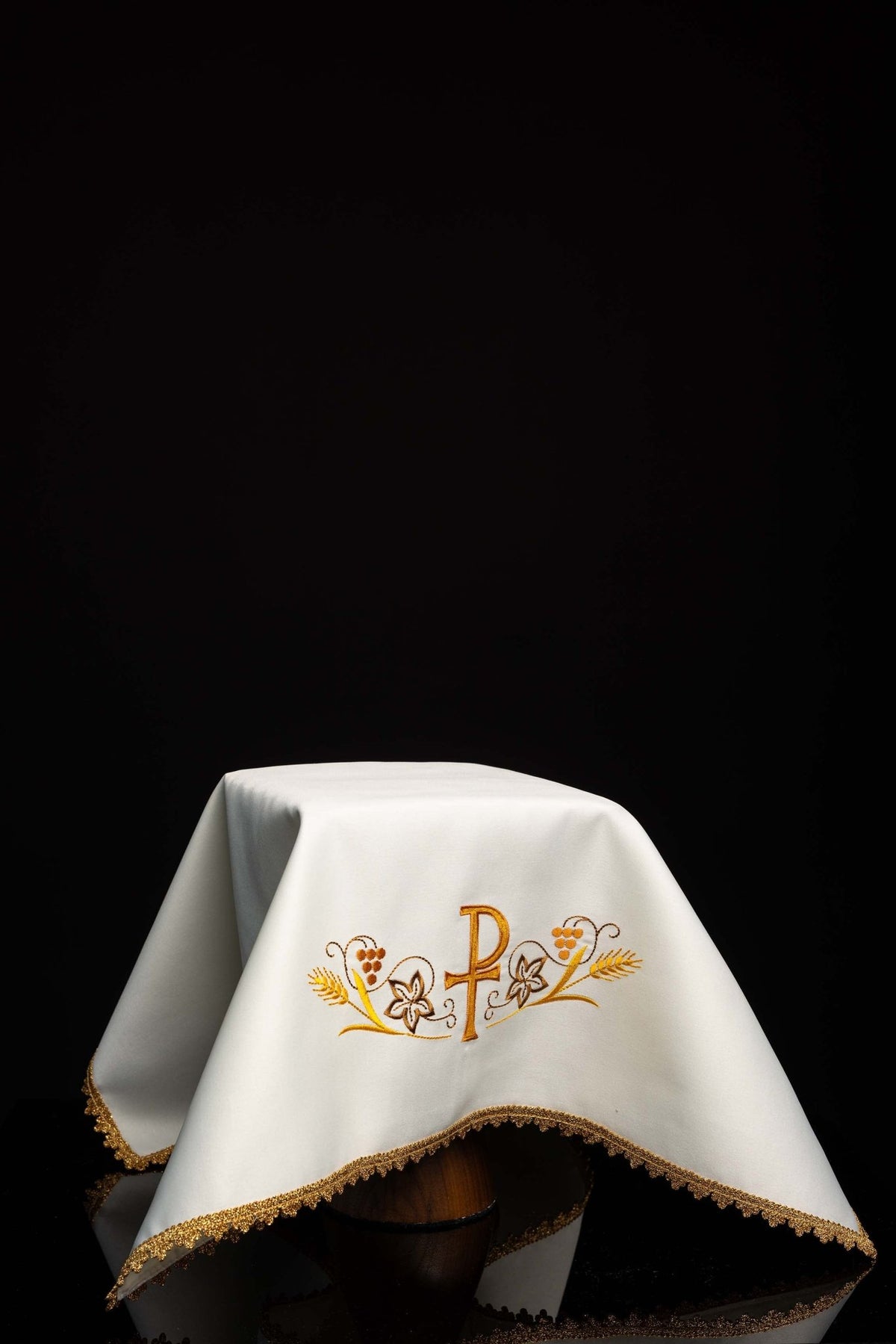 Worn view of a white chalice veil with embroidered PAX motif and gold trim