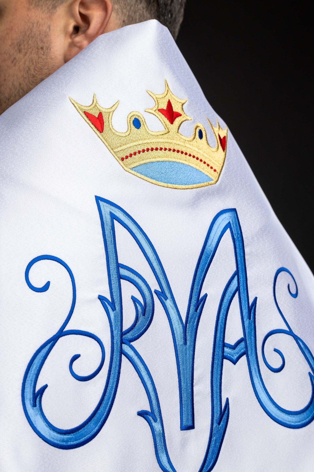 Close-up of the white humeral veil showing embroidered blue Marian monogram and crown